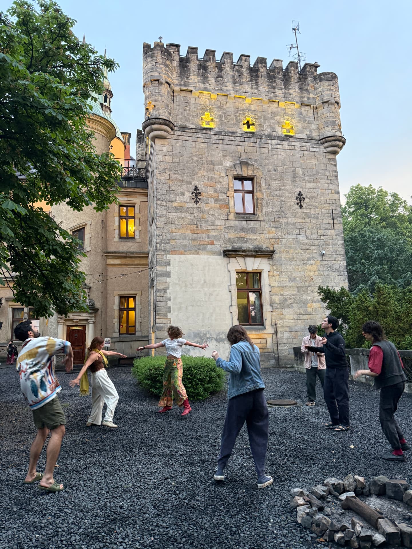 A group moving together in a castle courtyard at dusk, arms wide