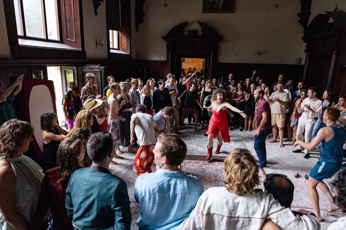 Kate Russell in a red dress, arms wide, in the middle of a full room