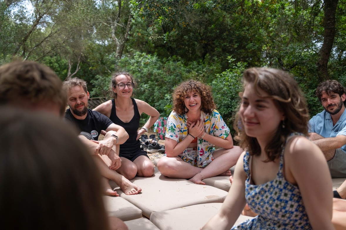 A circle of people seated outdoors, laughing mid-session