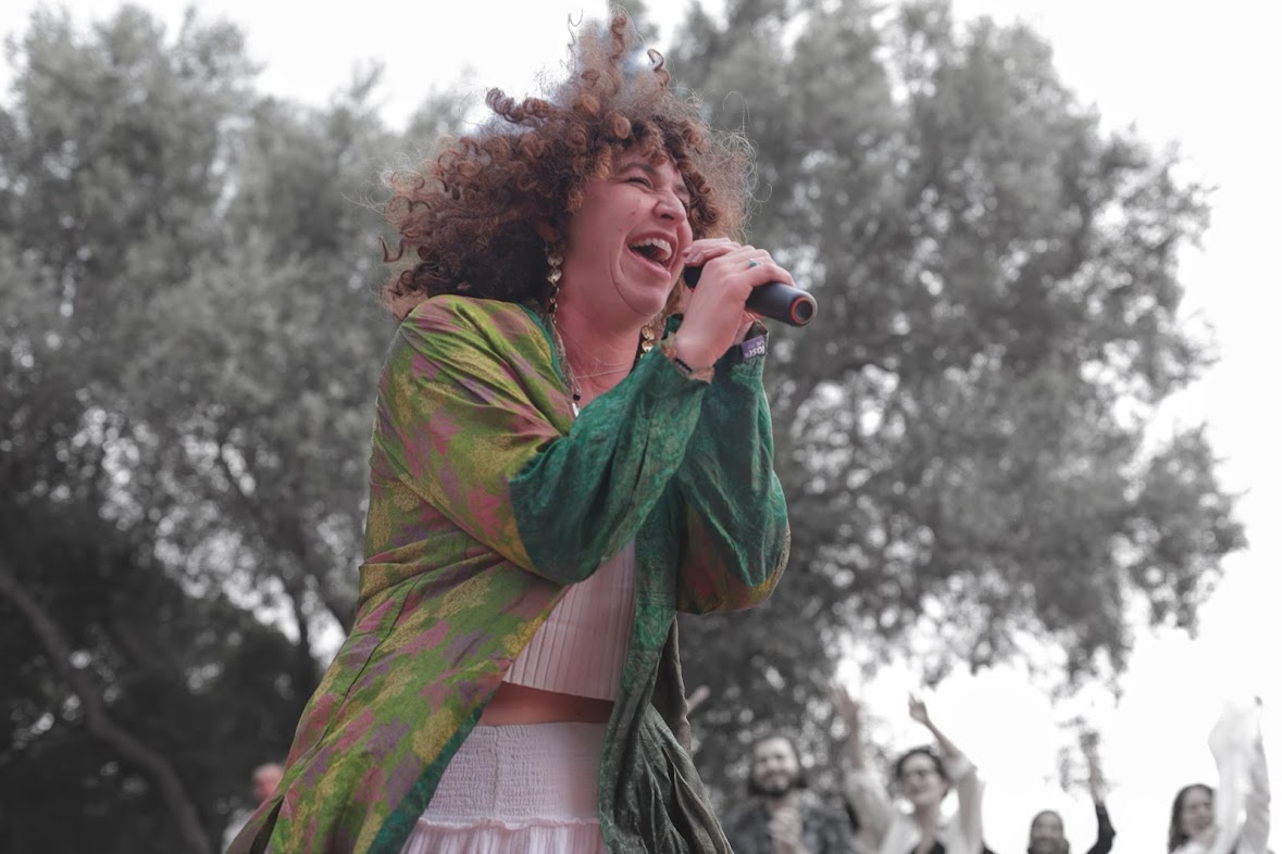 Kate Russell singing into a microphone on a hilltop as the crowd raises their hands